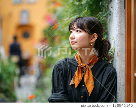 一位年輕女子站在綠樹和鮮花環繞的街角的肖像 128945140