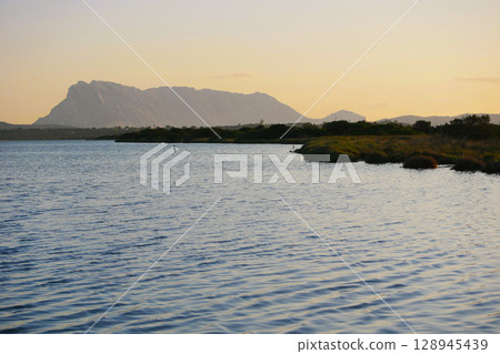 Scenic view of a mountainous landscape with a lake in the foreground during the sunset in San Teodoro, Sardinia, Italy Scenic view of a mountainous landscape with a lake in the foreground during the sunset in San Teodoro, Sardinia, Italy 128945439
