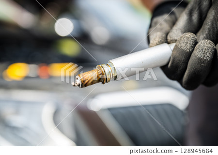 Used spark plug held by mechanic in glove during car engine maintenance 128945684