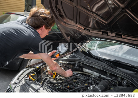 Mechanic using diagnostic tool to inspect car engine during vehicle maintenance Mechanic using diagnostic tool to inspect car engine during vehicle maintenance 128945688