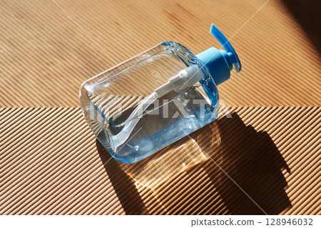 Hand washing gel in a blue bottle with a dispenser on a beige fluted background. Hand washing gel in a blue bottle with a dispenser on a beige fluted background. 128946032