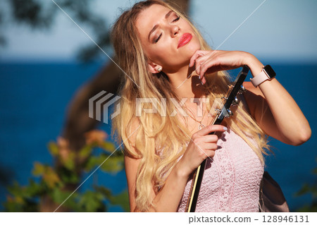 Blonde woman with acoustic guitar on seaside Blonde woman with acoustic guitar on seaside 128946131
