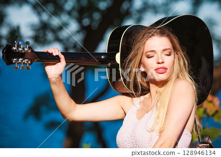 Blonde woman with acoustic guitar on seaside 128946134