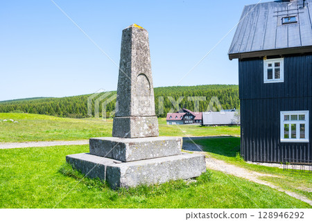 A stone pyramid stands tall in Jizerka Village, surrounded by lush green fields and mountains. Clear blue skies add to the serene atmosphere, revealing the charm of Czechia's countryside. A stone pyramid stands tall in Jizerka Village, surrounded by lush green fields and mountains. Clear blue skies add to the serene atmosphere, revealing the charm of Czechia's countryside. 128946292