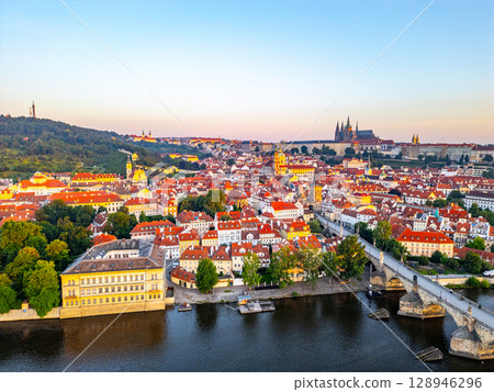 A breathtaking view of Prague at sunrise, showcasing the tranquil Vltava River and the iconic Charles Bridge with illuminated medieval buildings. This aerial perspective captures the city's beauty. A breathtaking view of Prague at sunrise, showcasing the tranquil Vltava River and the iconic Charles Bridge with illuminated medieval buildings. This aerial perspective captures the city's beauty. 128946296
