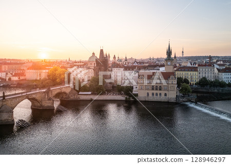 Sunrise casts a warm glow over Charles Bridge and the Vltava River in Prague, highlighting the city's rich architecture and serene atmosphere. A breathtaking aerial view showcases the old town. Sunrise casts a warm glow over Charles Bridge and the Vltava River in Prague, highlighting the city's rich architecture and serene atmosphere. A breathtaking aerial view showcases the old town. 128946297