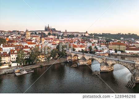 Bright colors fill the sky as the sun rises over Prague, illuminating the Vltava River and its medieval architecture. 128946298