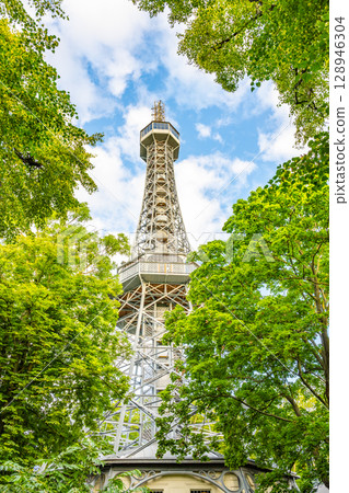 Petrin Lookout Tower rises above the lush trees in Prague, Czech Republic. Visitors can enjoy stunning views from the top, showcasing the city's skyline and natural beauty. Petrin Lookout Tower rises above the lush trees in Prague, Czech Republic. Visitors can enjoy stunning views from the top, showcasing the city's skyline and natural beauty. 128946304