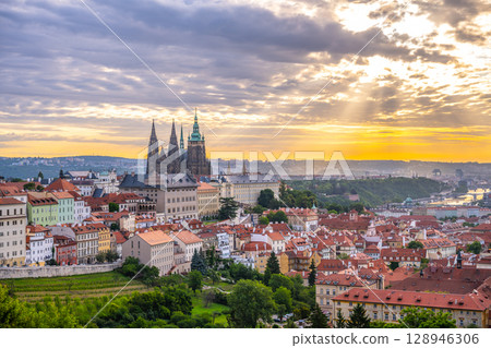 The sun rises over Prague Castle, illuminating the historic buildings and rooftops of the city. Soft clouds drift in the sky, creating a serene atmosphere in this enchanting location. The sun rises over Prague Castle, illuminating the historic buildings and rooftops of the city. Soft clouds drift in the sky, creating a serene atmosphere in this enchanting location. 128946306