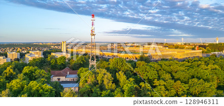 Great Strahov Stadium stands prominent in Prague, surrounded by lush greenery. This historic venue showcases its architecture against a backdrop of a vibrant sunset sky, capturing the city's essence. 128946311