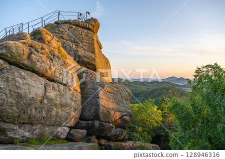 Evening sunlight casts a warm glow on the sandstone rocks of Popov Cliffs in Czechia, showcasing the stunning natural landscape of the Lusatian Mountains as the day comes to a close. 128946316