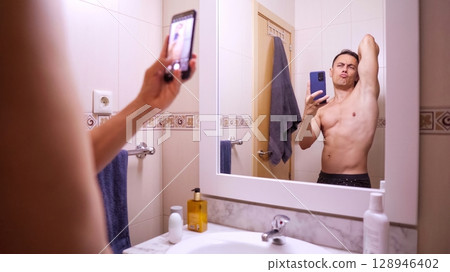 Man taking mirror selfie in bathroom 128946402