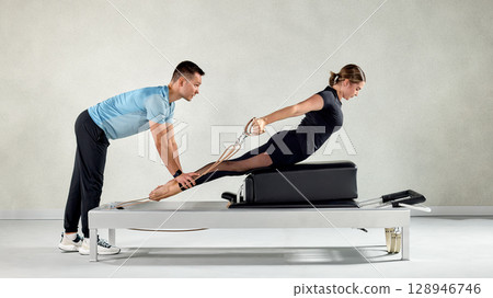 Fitness instructor assisting a Pilates session on a reformer machine 128946746