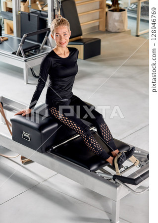 Woman practicing pilates on a reformer machine in a bright fitness studio 128946769