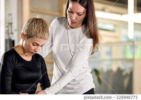 Female trainer assisting gym session indoors with a focused client 128946771