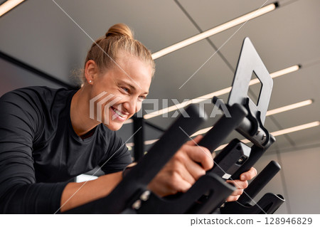 Smiling woman exercising indoors on a modern stationary bike, enjoying her workout 128946829