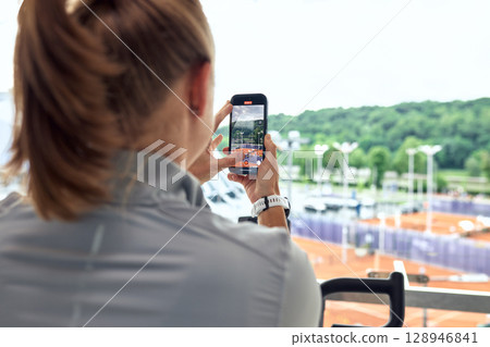 Woman capturing outdoor tennis courts with her smartphone from an elevated location 128946841