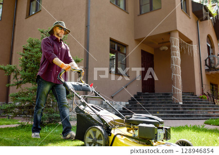 Man mowing the lawn outside a modern house in bright sunny weather 128946854