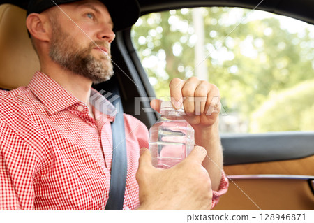 Man opening a water bottle while seated inside a modern vehicle Man opening a water bottle while seated inside a modern vehicle 128946871