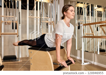 Woman Practicing Pilates on Chair Equipment in a Fully Equipped Studio 128946955
