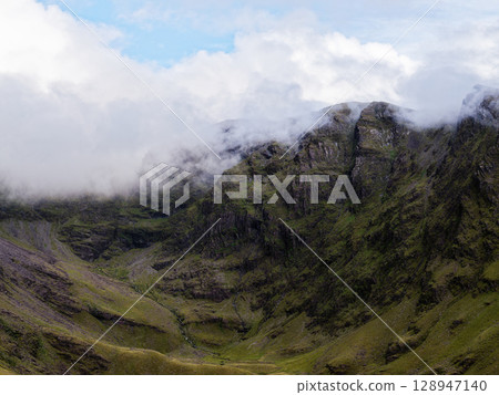 Rugged mountains and deep valleys define the terrain. Clouds obscure the peaks of coomloughra horseshoe, a popular hiking destination in County Kerry, Ireland. Rugged mountains and deep valleys define the terrain. Clouds obscure the peaks of coomloughra horseshoe, a popular hiking destination in County Kerry, Ireland. 128947140