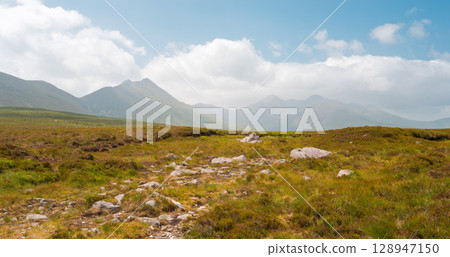 A grassy landscape with some rocks in the near distance and mountains in the far distance, under a cloudy sky. It is in Strickeen, which is in County Kerry, Ireland. 128947150