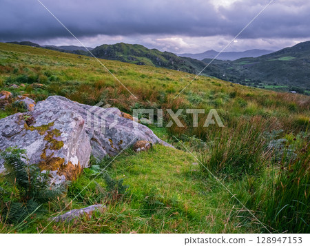 Scenic landscape of Coomloughra Horseshoe on an overcast day in County Kerry, Ireland, with green hills and cloudy skies. 128947153