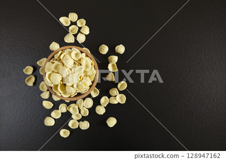 Orecchiette pasta in wooden bowl on black worktop. view from top. flat lay. copy space. Orecchiette pasta in wooden bowl on black worktop. view from top. flat lay. copy space. 128947162