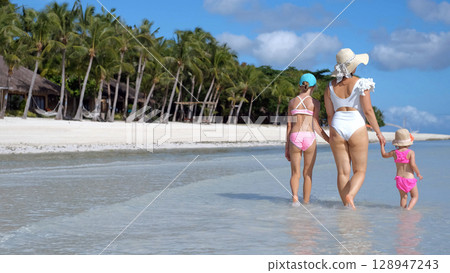 Rear view of mom and daughters walking in warm ocean water on sunny tropical beach Rear view of mom and daughters walking in warm ocean water on sunny tropical beach 128947243