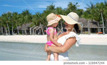 Mom embracing with baby daughter while relaxing in ocean on tropical beach Mom embracing with baby daughter while relaxing in ocean on tropical beach 128947244