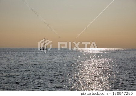 Sailboat silhouette on calm sea at golden hour sunset 128947290