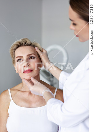 Facial plastic surgeon preparing patient for facelift surgery in medical clinic. Cosmetic face lifting procedure consultation, anti-aging operation for wrinkle correction and facial skin tightening 128947316
