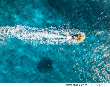 Aerial view of a yellow jetski sailing fast on turquoise water Aerial view of a yellow jetski sailing fast on turquoise water 128947330