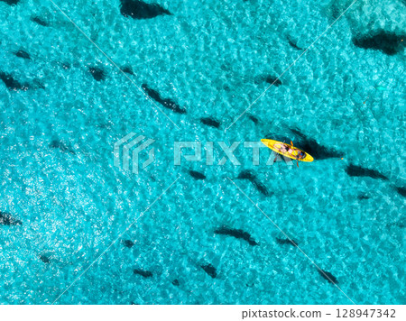 Aerial view of a kayakers paddling through vibrant blue waters Aerial view of a kayakers paddling through vibrant blue waters 128947342