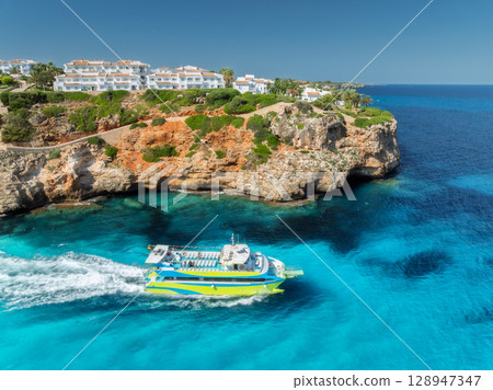 Aerial view of green yacht, sea with turquoise water, rocky coast 128947347
