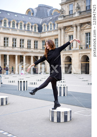 Young woman balancing playfully on striped column in Paris 128947425