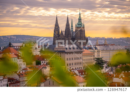 As the sun rises, Prague Castle stands majestically against the colorful sky. The historic architecture of the castle is beautifully illuminated, reflecting the dawn's serene ambiance over the city. As the sun rises, Prague Castle stands majestically against the colorful sky. The historic architecture of the castle is beautifully illuminated, reflecting the dawn's serene ambiance over the city. 128947617