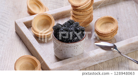 Close-up of black caviar in ceramic pot and mini tartlet placed on wooden board. Close-up of black caviar in ceramic pot and mini tartlet placed on wooden board. 128948063