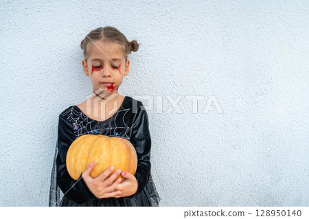 Child Holding Halloween Pumpkin With Spooky Makeup 128950140