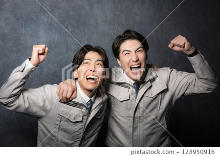 兩名身穿工作服的年輕男子在灰色背景下互相摟著拳頭慶祝 128950916