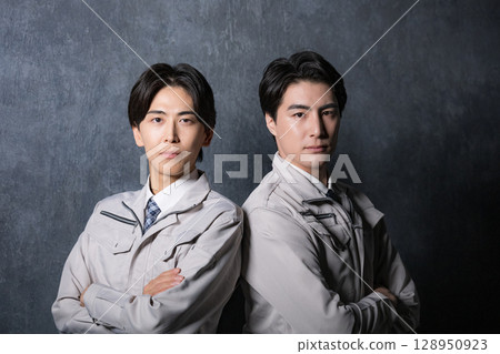兩名身穿工作服的男子背對背站著，在灰色背景下表情嚴肅地看著鏡頭 128950923