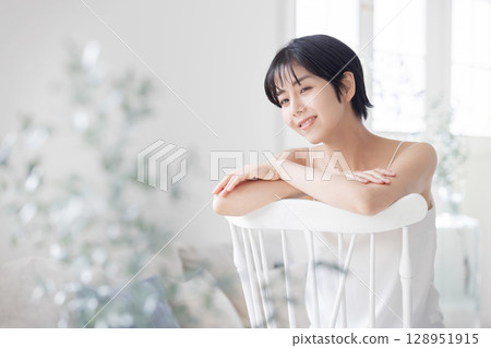 A young woman in a camisole sitting across a chair 128951915