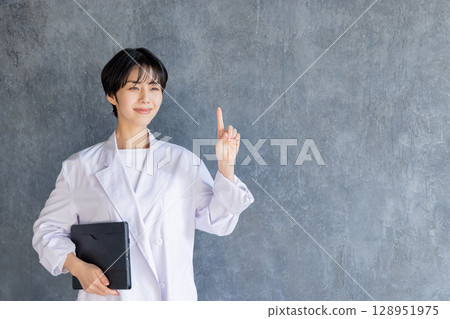 A young woman in a white coat pointing 128951975