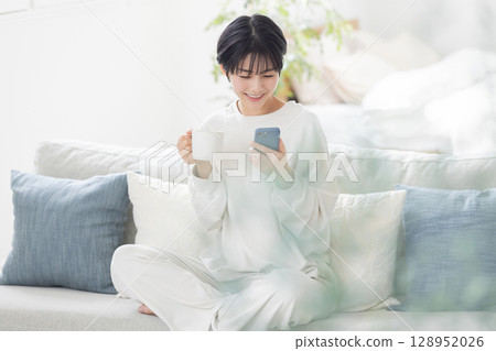 一位身穿睡衣的女士正在操作智慧型手機 一位身穿睡衣的女士正在操作智慧型手機 128952026