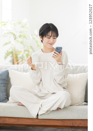 A woman in pajamas operating a smartphone 128952027
