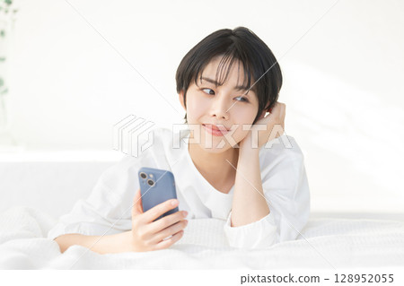 A woman lying in bed and using her smartphone A woman lying in bed and using her smartphone 128952055