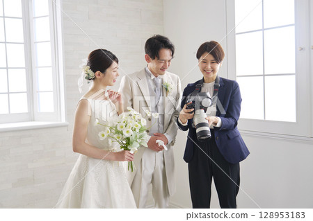 Smiling bride and groom and bridal photographer talking Smiling bride and groom and bridal photographer talking 128953183