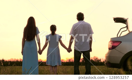 The child holds the father and mother by the hand. Traveling by car. family car. a team of people. People are a family in nature. A man, a woman and a child, holding hands, look at the sunset. The 128953257