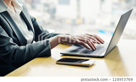 一位女性商務人士在辦公室使用筆記型電腦和智慧型手機工作,背景是一座城市 一位女性商務人士在辦公室使用筆記型電腦和智慧型手機工作,背景是一座城市 128953769