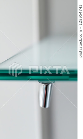 A glass shelf with a metal bracket on the top 128954743